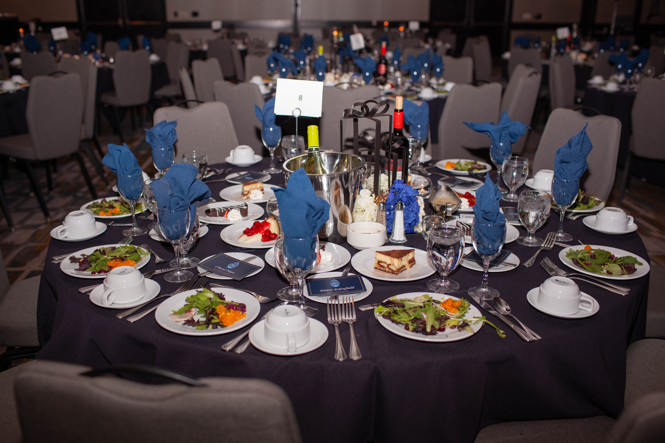 Black-tie gala tables set with blue napkins, floral arrangements and place settings